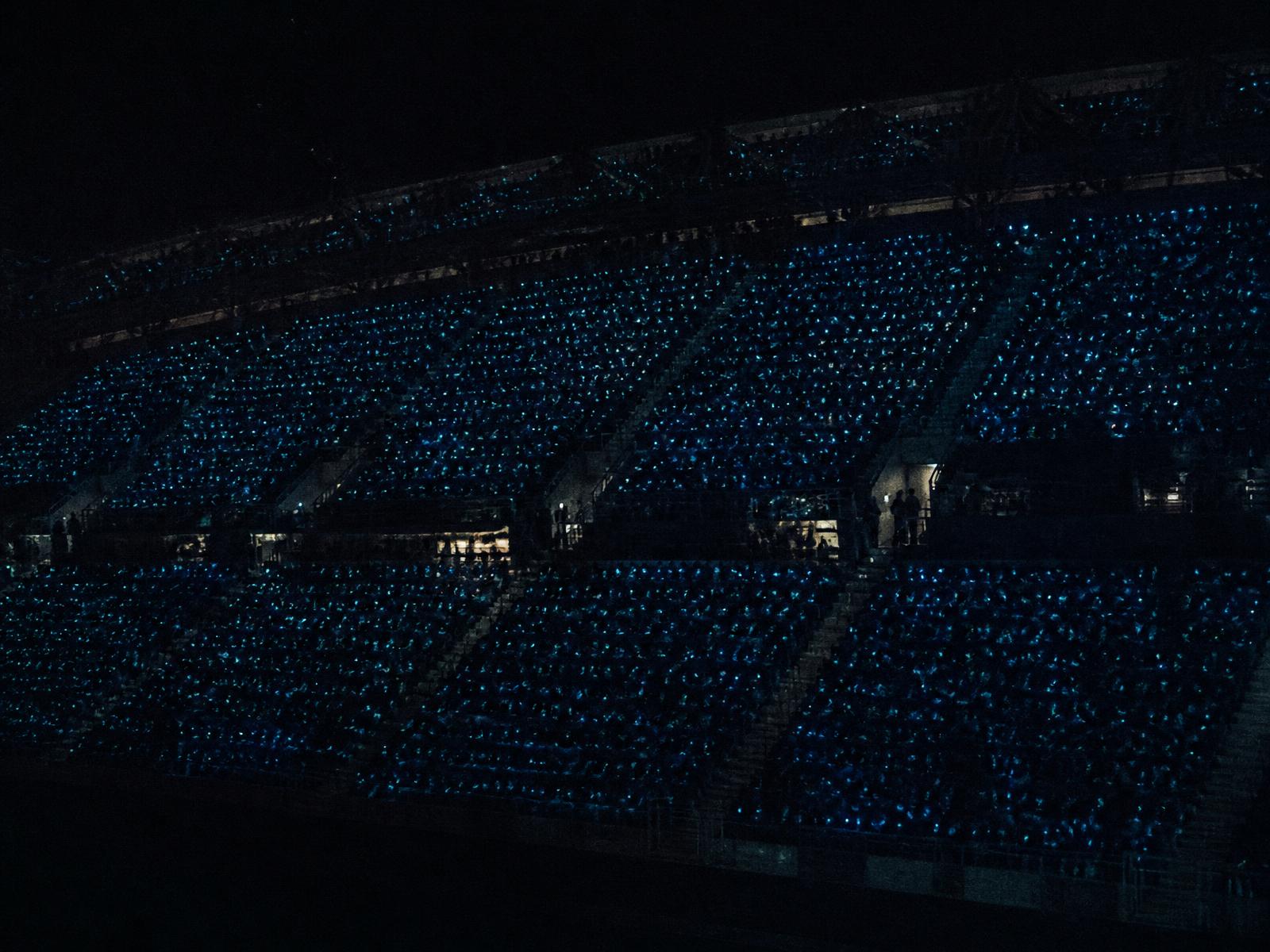 A stadium seating block where hundreds of illuminated jerseys resolve into individual points of light